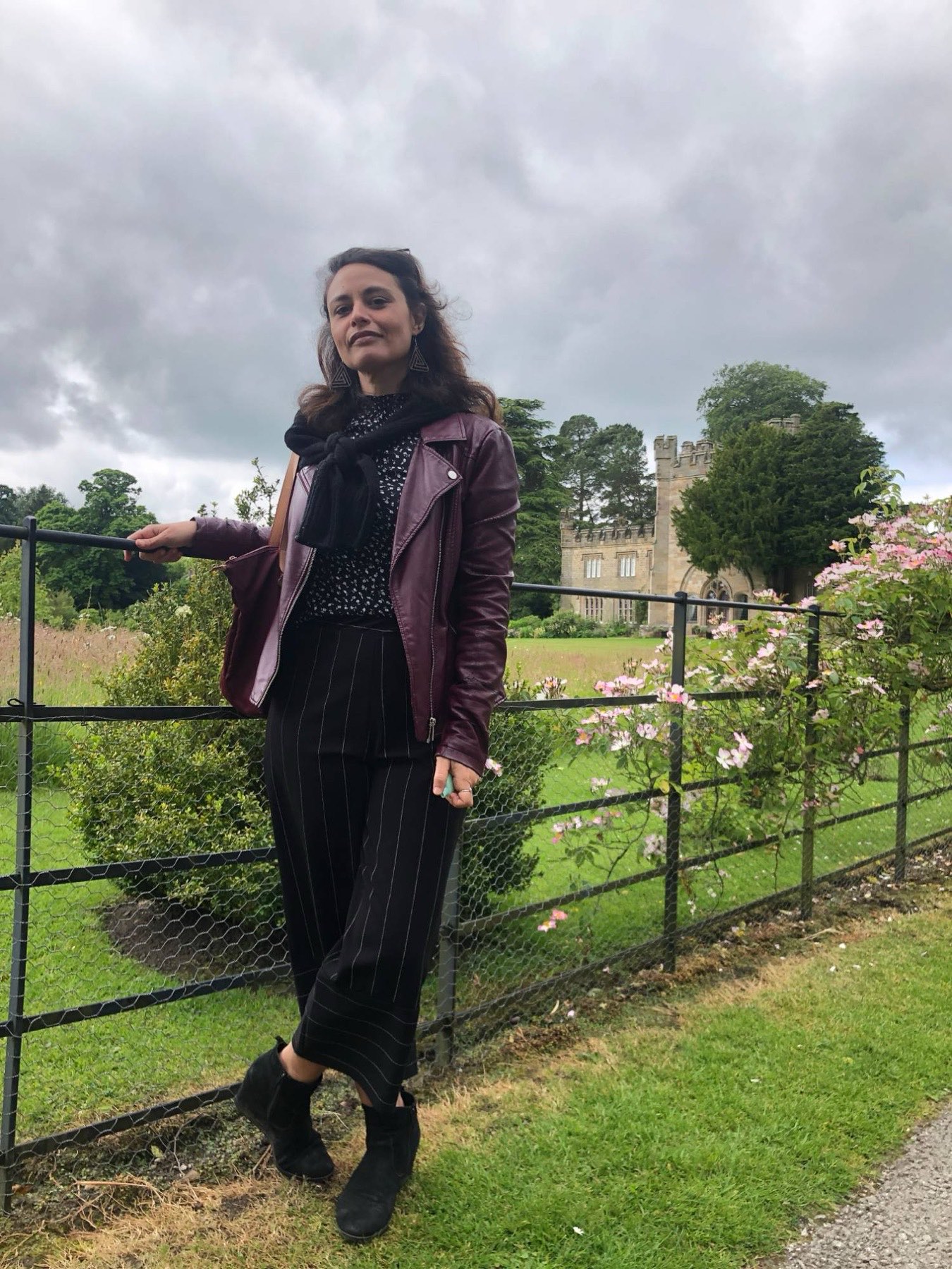Ines in a burgundy leather jacket leaning on a garden railing