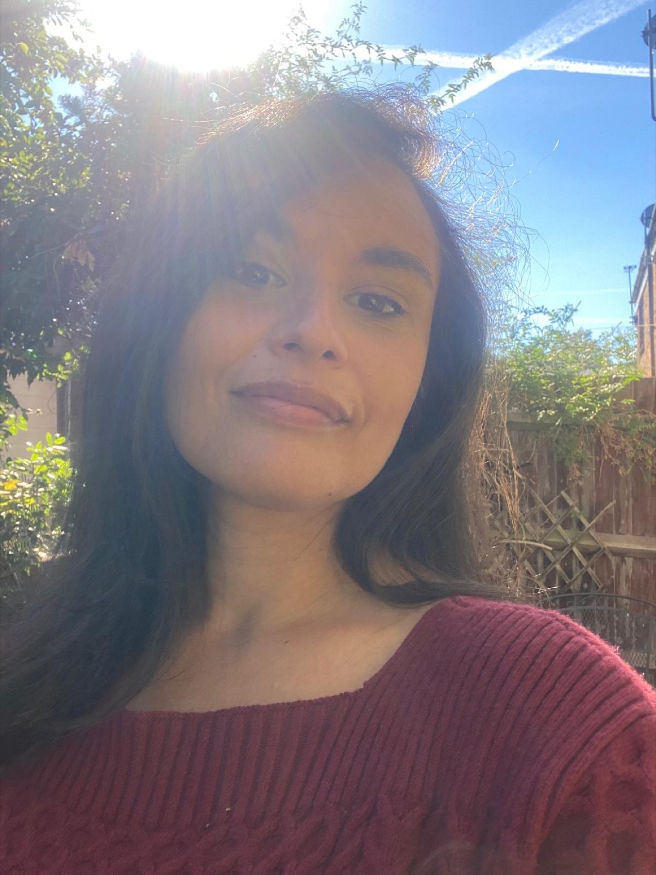 Ines smiling in the sunshine, in a red jumper