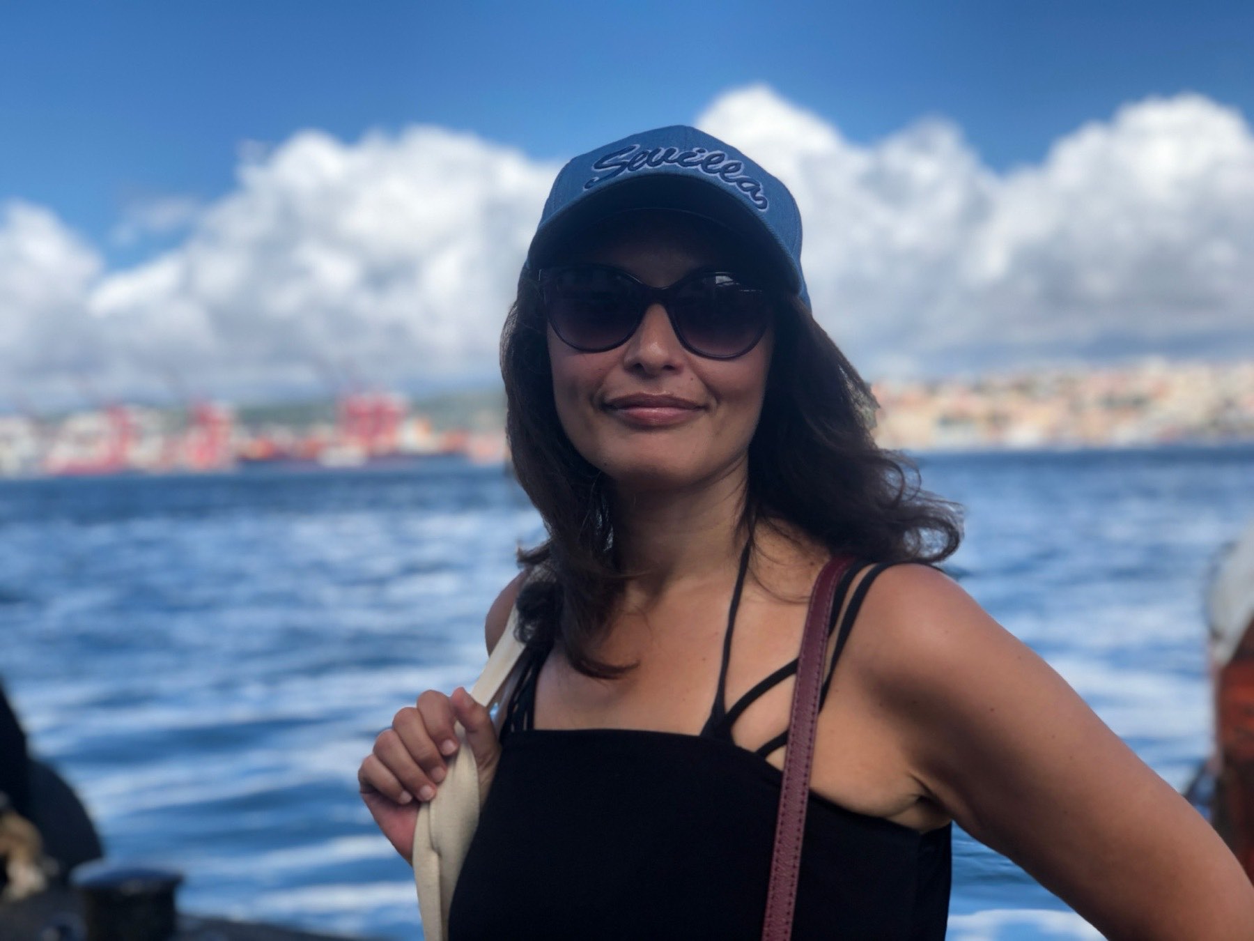 Ines in a cap and sunglasses by the water on a bright day