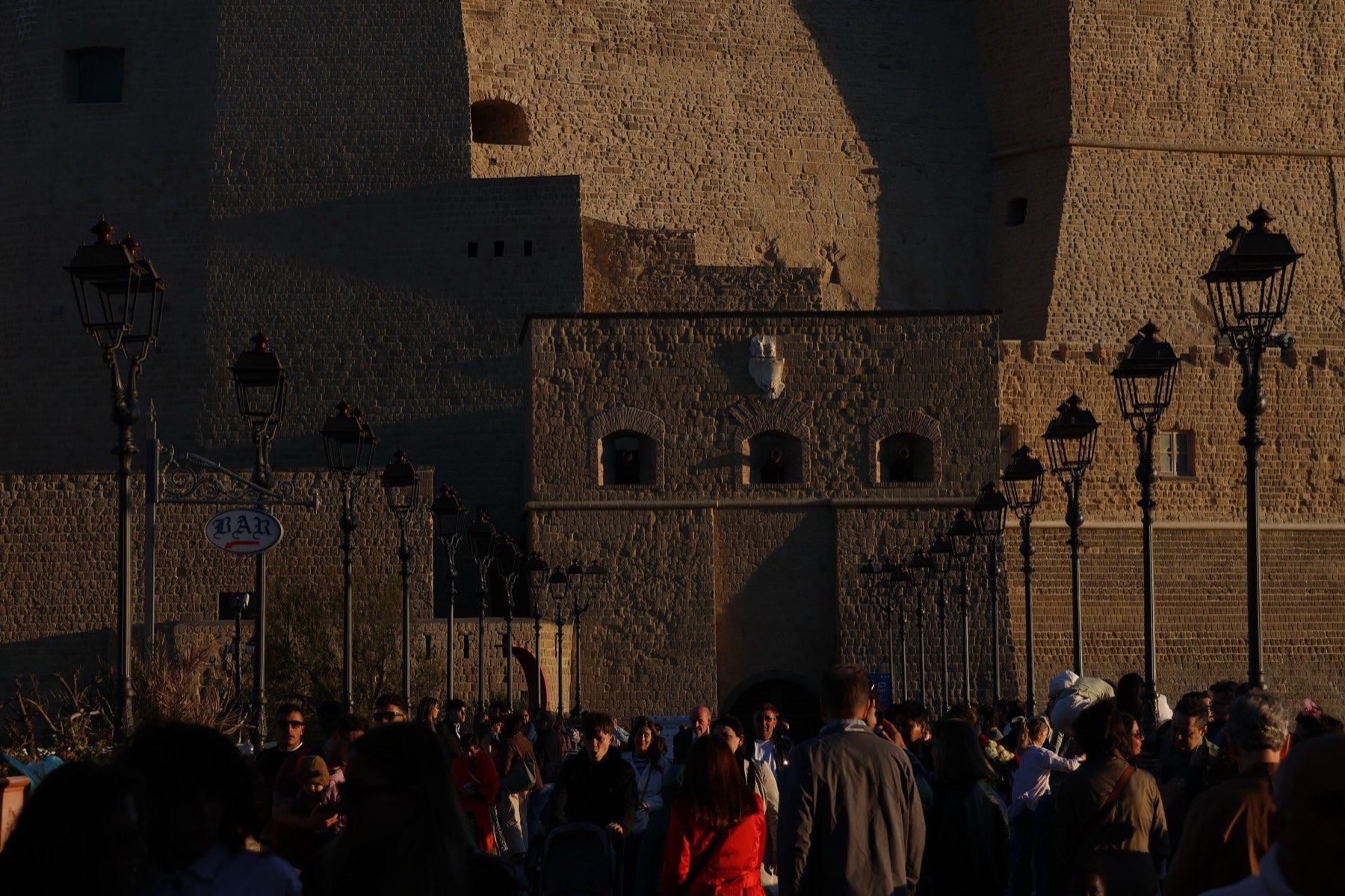 People walking at sunset beneath the walls of Castel dell'Ovo