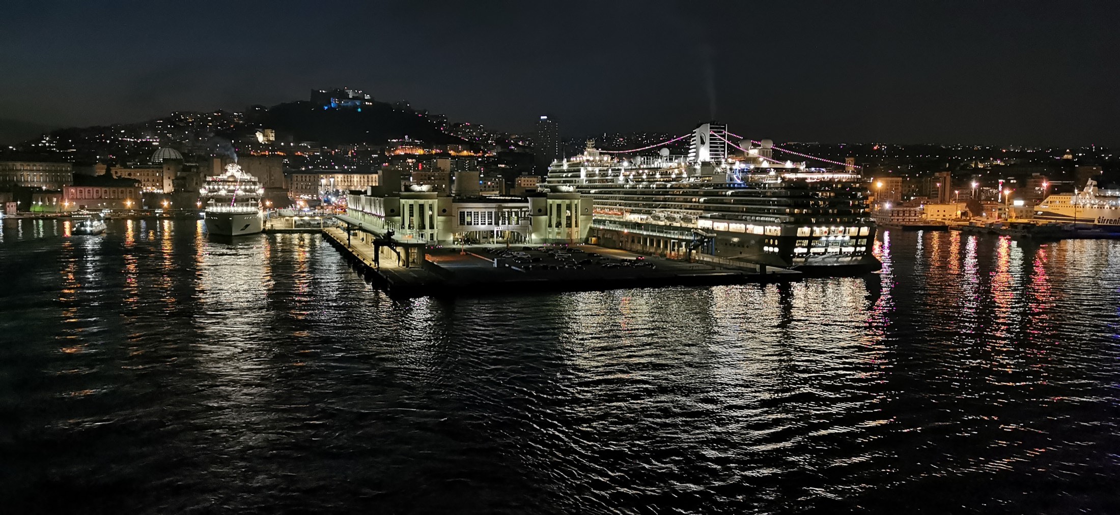 Naples harbour at night, the city lights reflected in the water and Castel Sant'Elmo lit on the hill