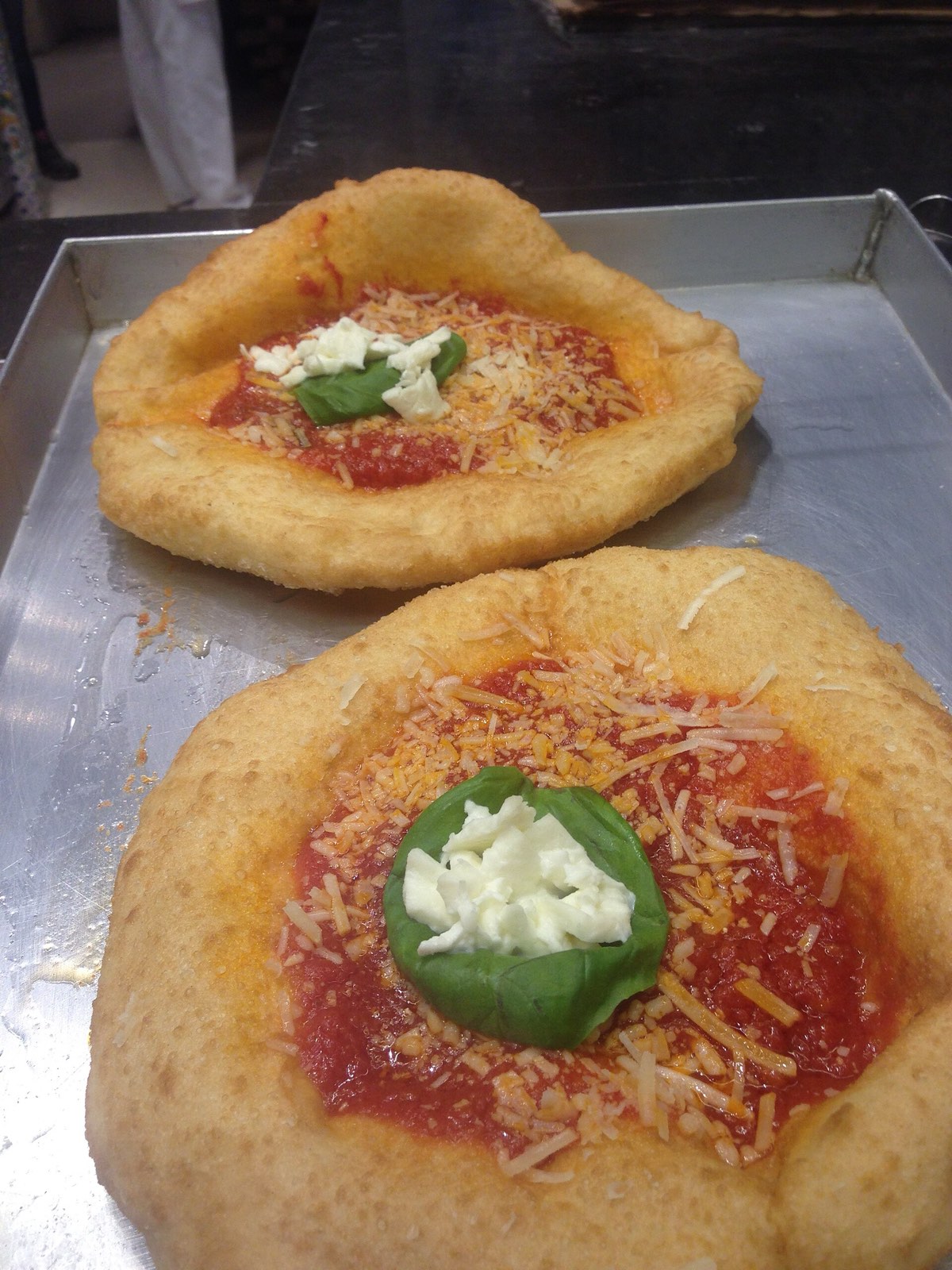 Two small fried pizzas topped with tomato, cheese and basil