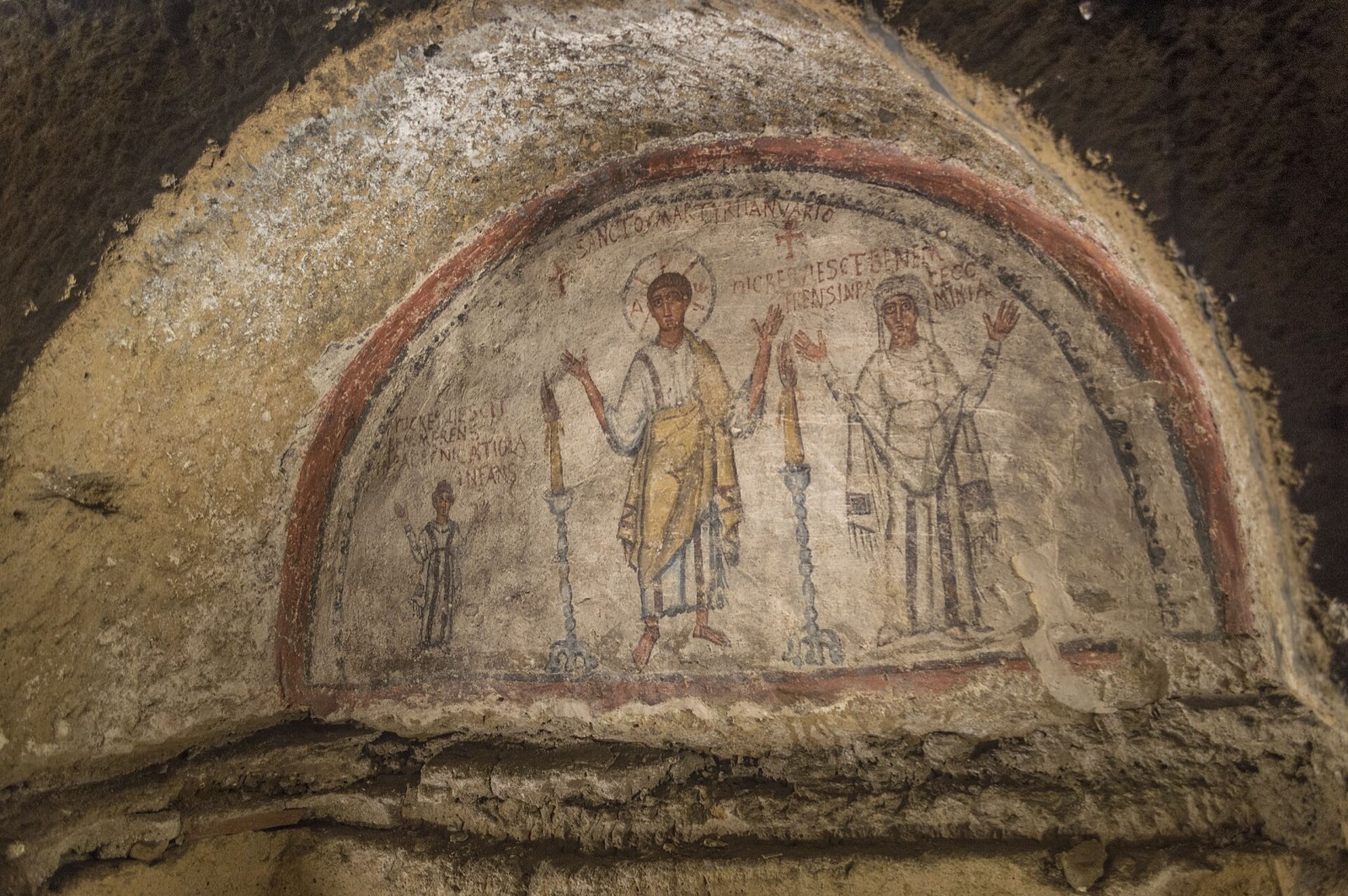 An ancient fresco of saints painted in an arched niche in the catacombs of San Gennaro
