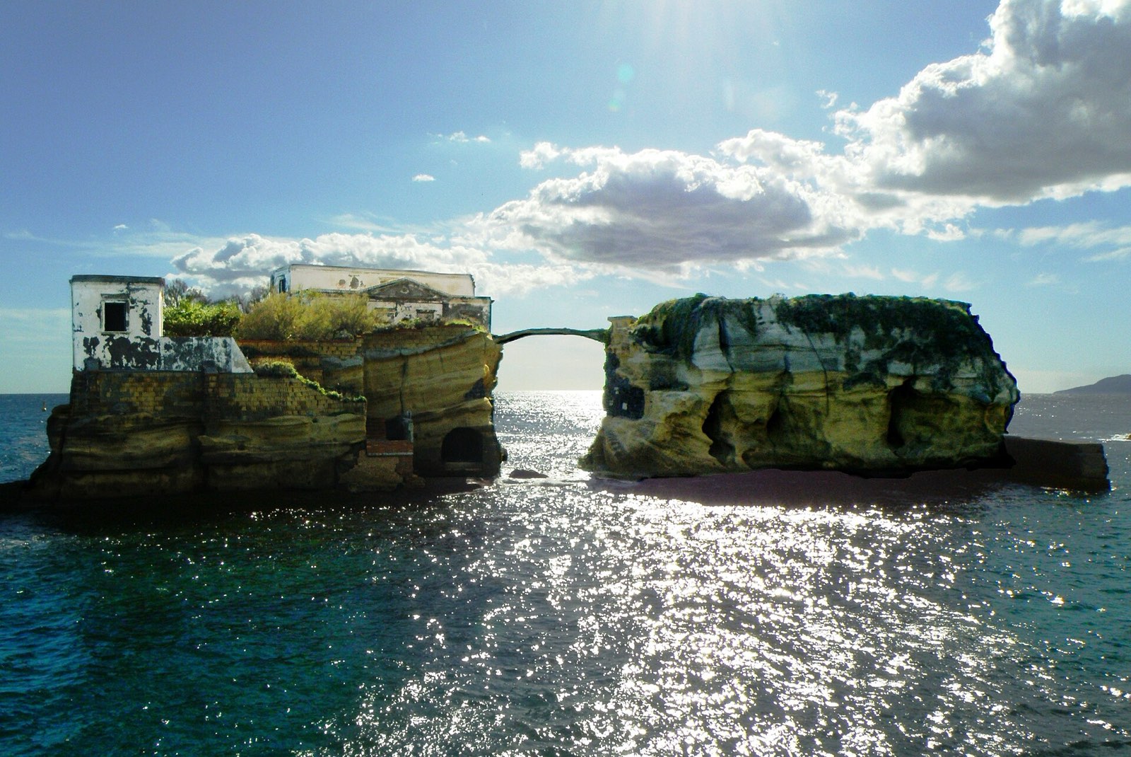 The two small islets of La Gaiola joined by a little stone bridge, with sun glittering on the sea