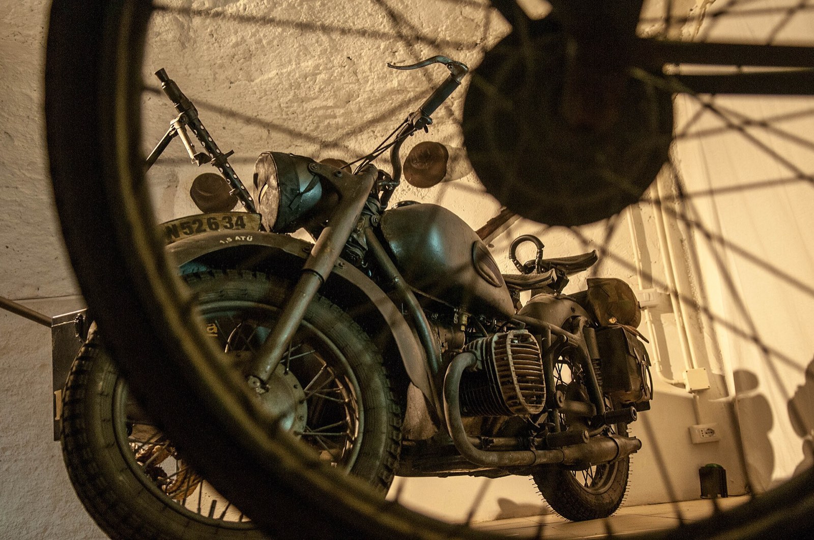 An old motorbike resting in the stone tunnels of the Galleria Borbonica, seen through a spoked wheel
