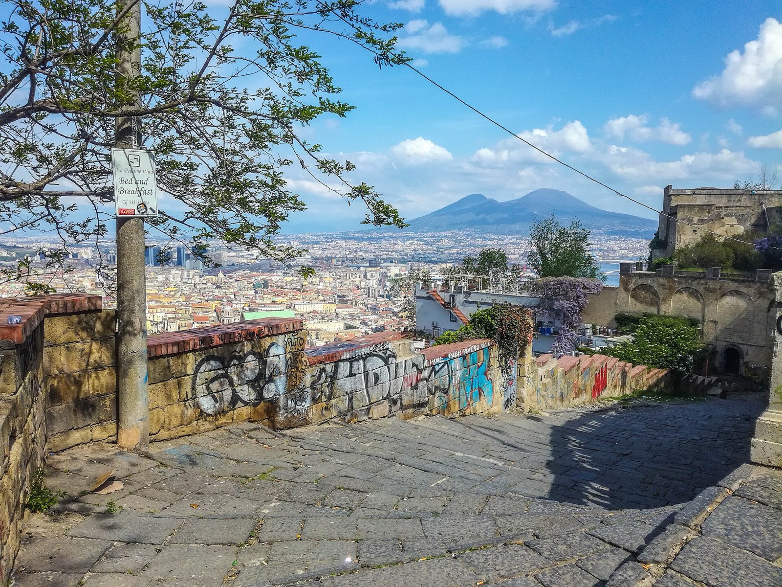 The stone steps of the Pedamentina descending towards the rooftops of Naples, with Vesuvius on the horizon