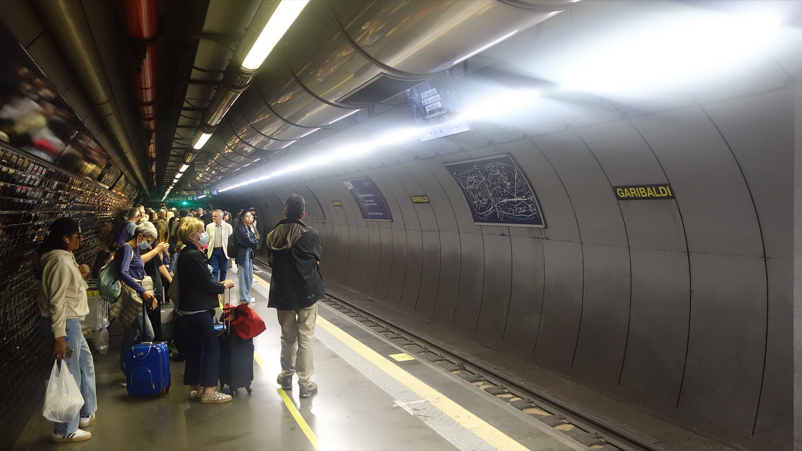 Travellers waiting on the curved, brightly lit platform at Garibaldi station