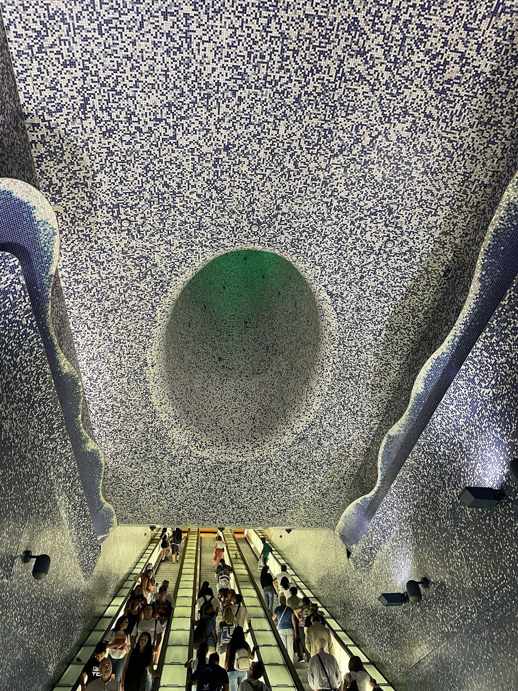 Looking up the escalators of Toledo metro station into a vast blue mosaic cone of light