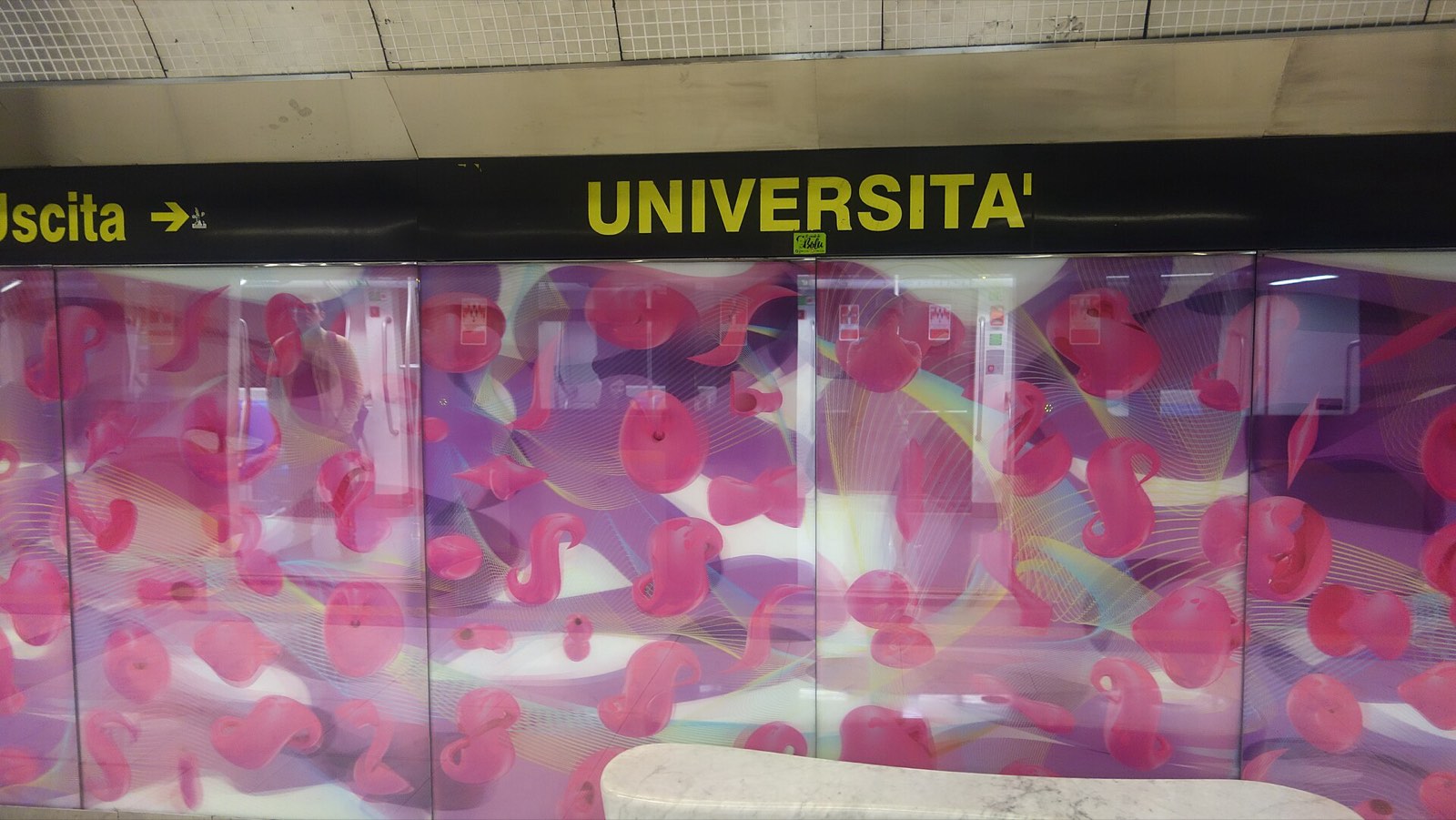 Bright pink and purple graphic glass panels along the platform at Università station